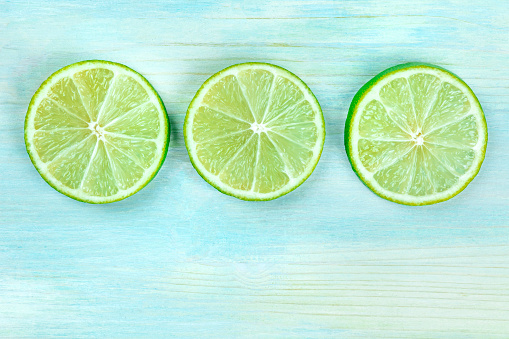 An overhead closeup photo of three lime slices on a teal blue background