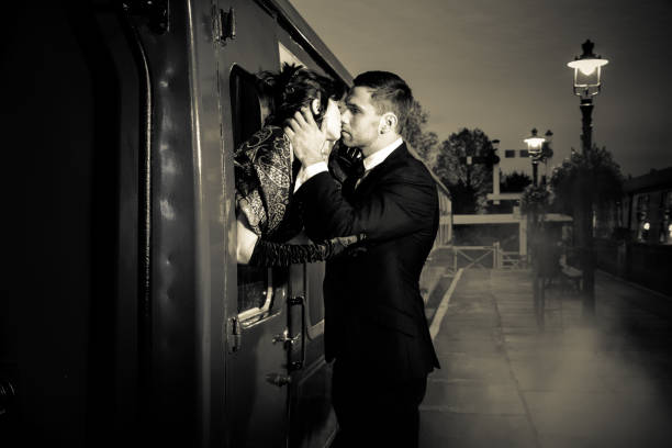 vintage pareja abrazándose y besándose en la plataforma de la estación de ferrocarril como de tren está a punto de salir - depart fotografías e imágenes de stock