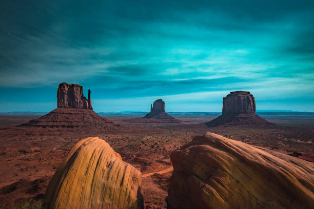 Classic panoramic view of scenic Monument Valley with the famous Mittens and Merrick Butte illuminated in beautiful mystic moonlight on a starry night in summer, Arizona, American Southwest, USA