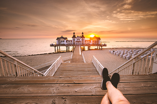 Young man sitting on wooden pier enjoying sunrise at Seebrucke Sellin, Baltic Sea, Germany
