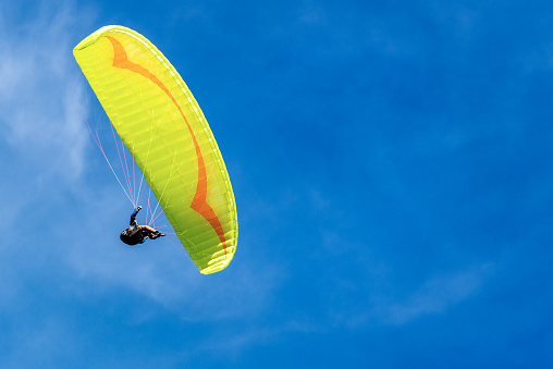 Yellow and orange paragliding on a blue sky with clouds on background