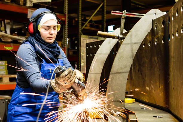 Young female trainee works with a grinder in a workshop, flying sparks