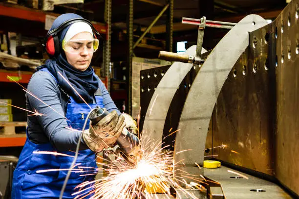 Photo of Young female trainee works with a grinder in a workshop, flying sparks