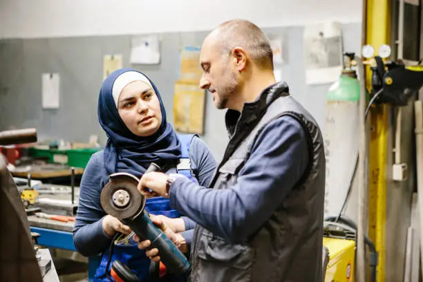 technician explains a grinder to a female trainee in a workshop
