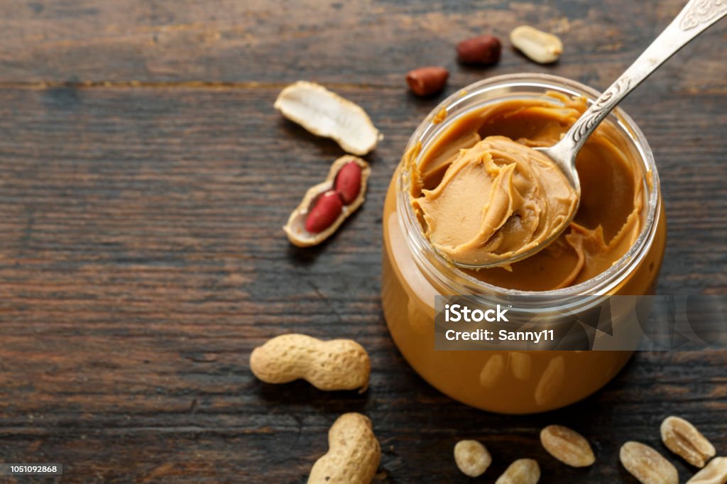 peanut paste in an open jar and peanuts peanut paste in an open jar and peanuts in the peel scattered on the table Peanut Butter Stock Photo