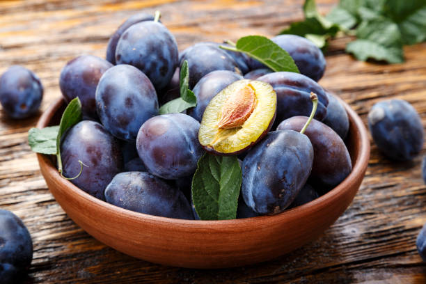 raw plums in a plate on a brown wooden background. raw plums in a plate on a brown wooden background. place for text plum stock pictures, royalty-free photos & images