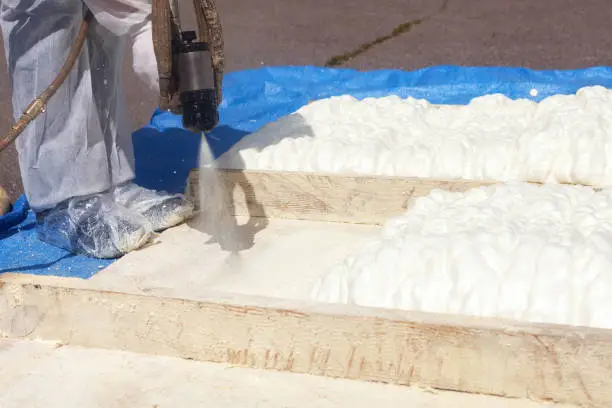 Photo of Technician spraying foam insulation using Plural Component Spray Gun. Spraying polyurethane foam for roof