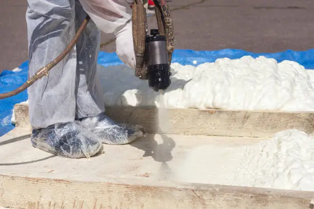 Photo of Technician spraying foam insulation using Plural Component Spray Gun. Spraying polyurethane foam for roof