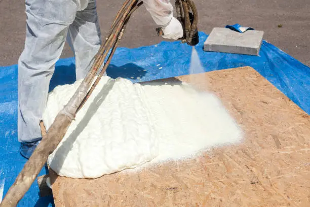 Photo of Technician spraying foam insulation using Plural Component Spray Gun. Spraying polyurethane foam for roof