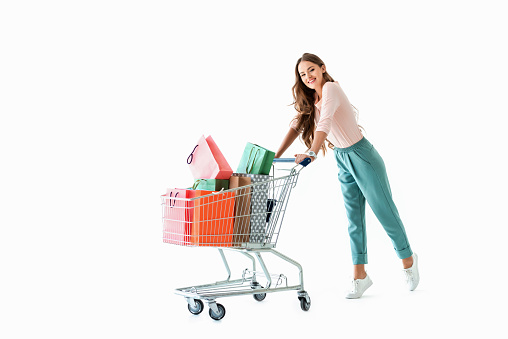 beautiful cheerful girl with shopping cart and bags, isolated on white