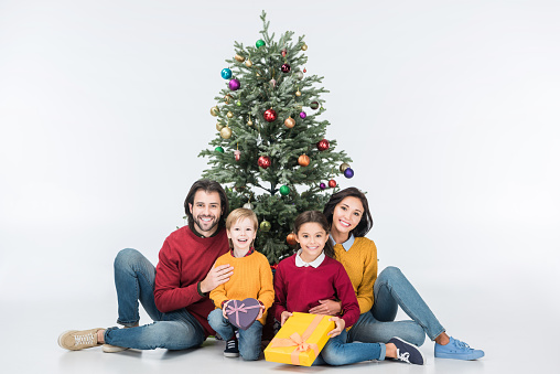 Happy family sitting near christmas tree with presents isolated on white