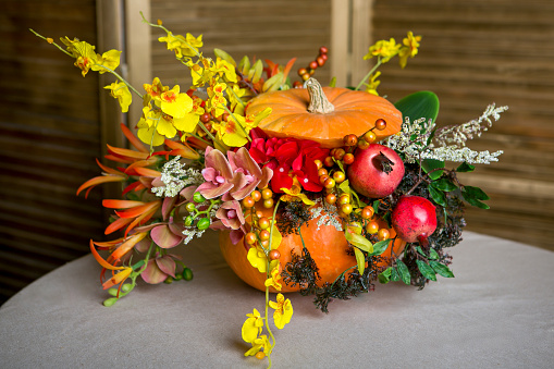 Bright autumn bouquet of orchids, pomegranates, tropical greenery, moss in a pumpkin on the background