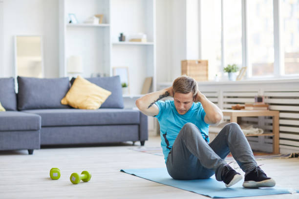 Sit-ups Young man in activewear sitting on the floor with his hands behind head and doing sit-ups exercise room photos stock pictures, royalty-free photos & images
