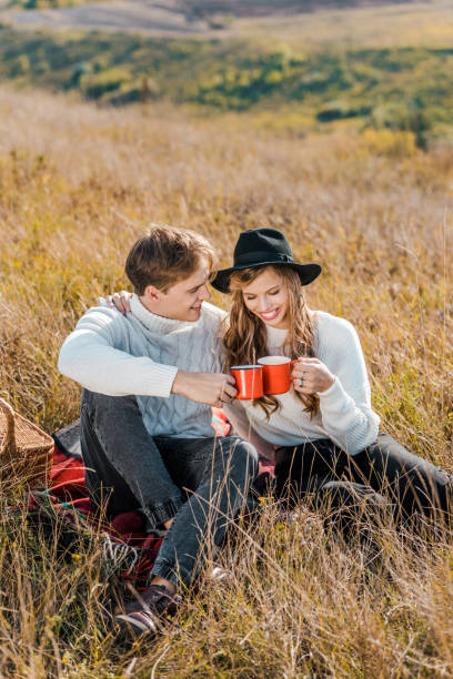 istock young smiling couple clinking with cups and relaxing on rural meadow 1051119986