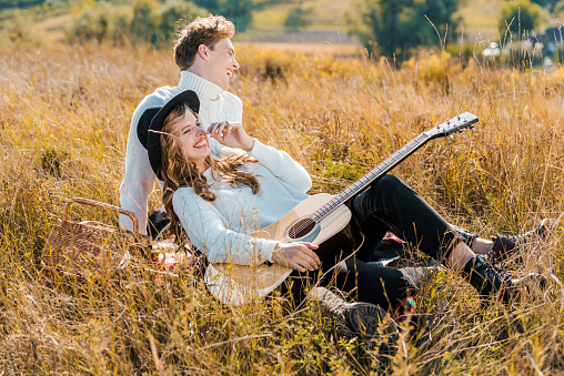happy young couple with guitar relaxing on meadow