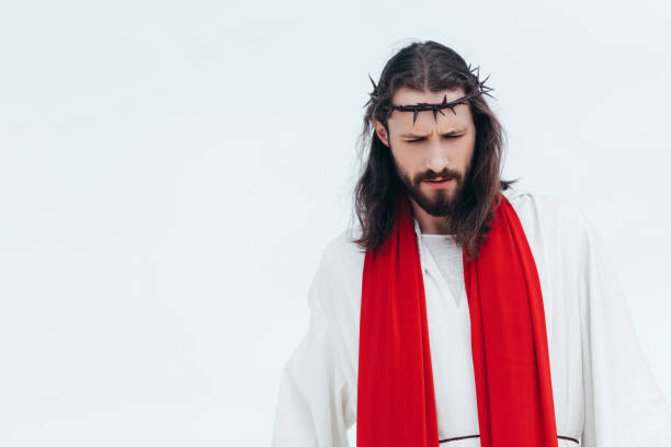 istock Jesus in robe, red sash and crown of thorns looking down against light sky 1051127912