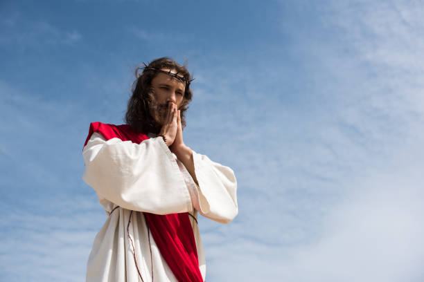 istock low angle view of Jesus in robe and red sash praying against blue sky 1051128020