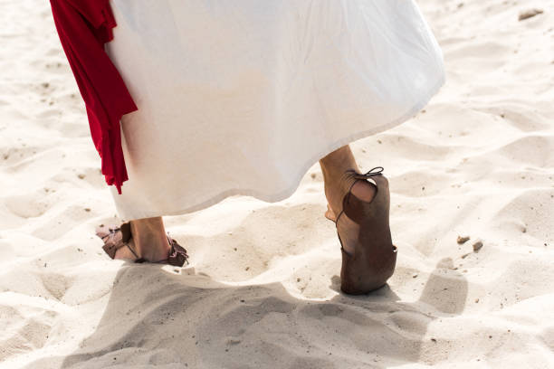 cropped image of Jesus in robe, sandals and red sash walking on sand in desert cropped image of Jesus in robe, sandals and red sash walking on sand in desert jesus christ stock pictures, royalty-free photos & images