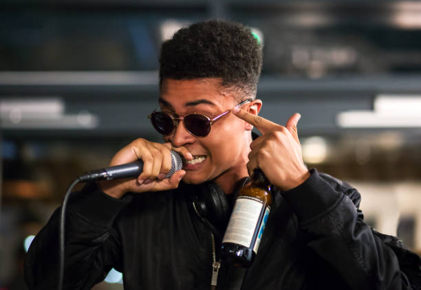 Black rapper performing with microphone, pointing to head. Bottle in hand. stock photo