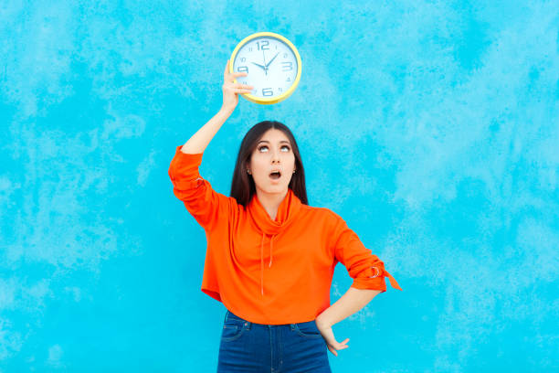 kobieta trzymająca zegar sprawdzanie czasu na niebieskim tle - checking the time time clock women zdjęcia i obrazy z banku zdjęć