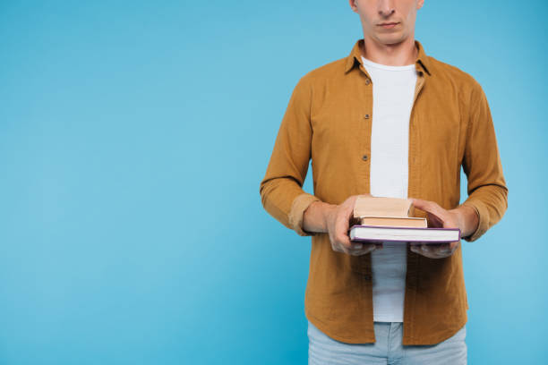istock cropped image of man holding three books isolated on blue 1051139316
