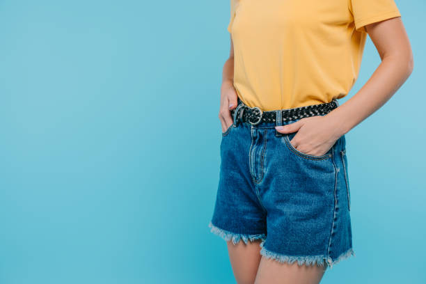 imagen recortada de niña de pie con las manos en bolsillos aislados en azul - jean shorts fotografías e imágenes de stock