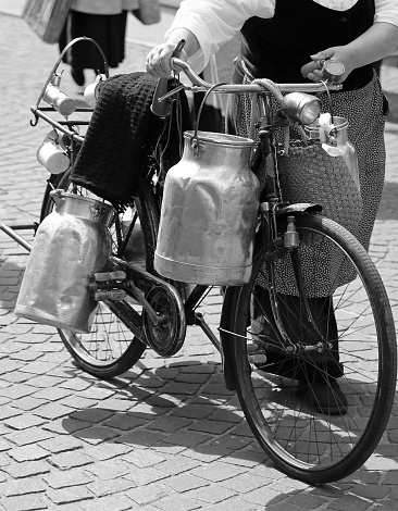 elderly woman carrying milk cans with an old rusty bicycle  and black and white effect
