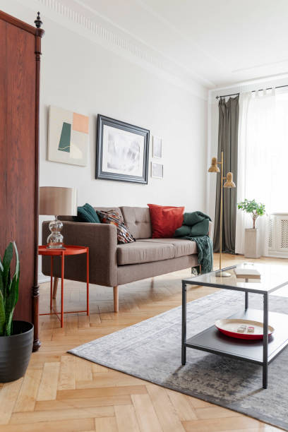 istock Lamp on table next to sofa in bright living room interior with posters and grey carpet. Real photo 1051151068