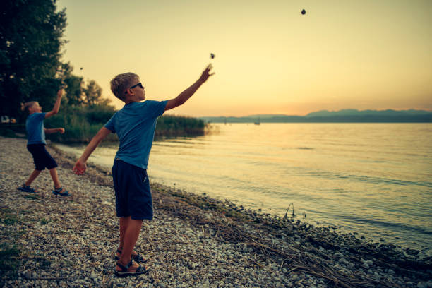 meninos jogando pedras no lago de garda, itália - throwing stone little boys child - fotografias e filmes do acervo