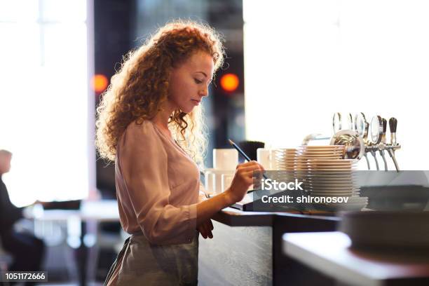 Pensive Waitress Adding Order In Restaurant Pos Stock Photo - Download Image Now - Point Of Sale, Restaurant, Order