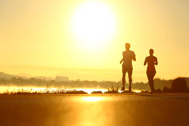 силуэты мужчины и женщины, бегущие на рассвете - family fun running couple стоковые фото и изображения