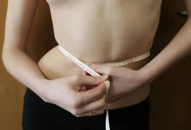 Slim girl is measuring her waist with a centimetre tape measure at home. Fit sport healthy photo. Successful diet.