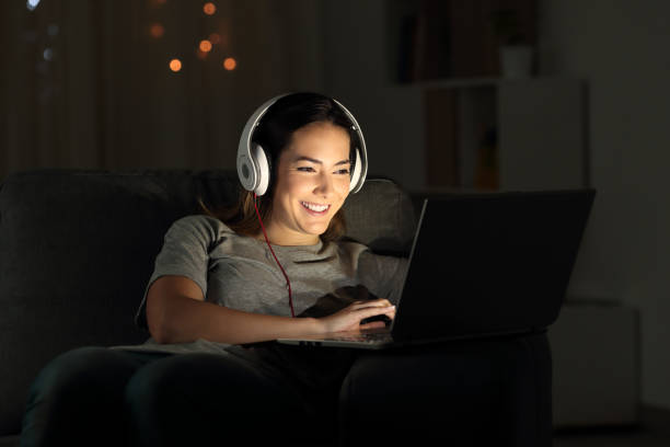 Happy girl elearning online with a laptop in the night sitting on a couch in the living room at home