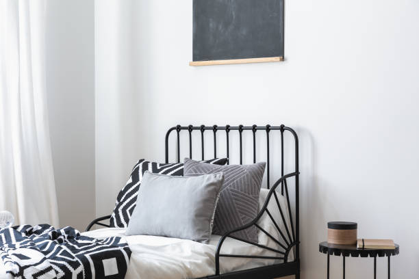 istock Grey pillows and patterned sheets on bed in white bedroom interior with black poster. Real photo 1051187680