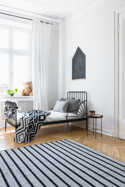 istock Striped carpet in white bedroom interior with patterned blanket on bed near window. Real photo 1051187686