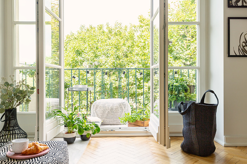 Puerta de cristal abierta de un interior de sala de estar en un jardín de la ciudad en un balcón soleado con plantas verdes y muebles cómodos photo