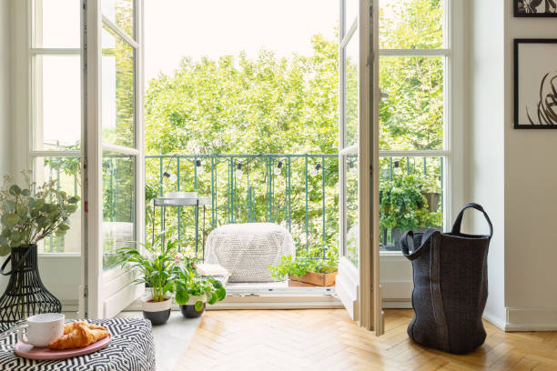 緑の植物と快適な家具と日当たりの良いバルコニーのシティ ガーデンにリビング ルームのインテリアから開いているガラス戸 - バルコニー ストックフォトと画像