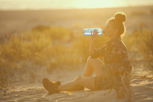 adventure traveller woman on seacoast at sunset drinking water