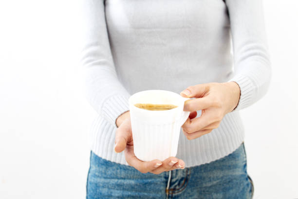 Female hand holding a white coffee cup on white wall background. Mock up, perfect for putting your design