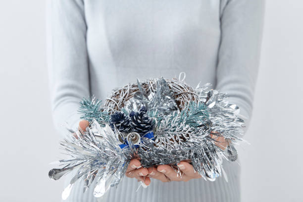 Female hand holding green Christmas wreath on white wall background. Mock up, perfect for putting your design