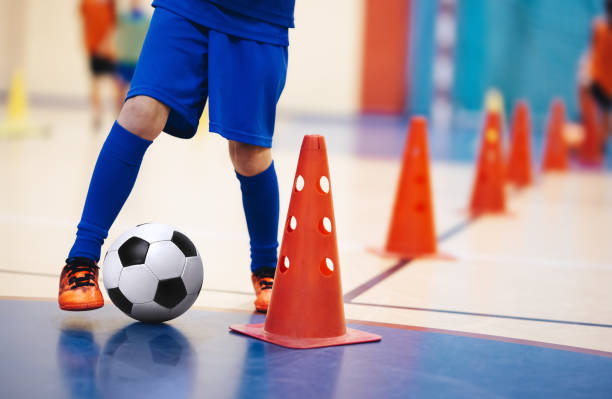 giocatori di calcio indoor che si allenano con le palle. palazzetto dello sport indoor. giocatore di calcio a 5 indoor, palla, pavimento futsal e cono rosso. trapano dribbling da allenamento a futsal. background sportivo. campionato di calcio a 5. - little boys people indoors soccer foto e immagini stock