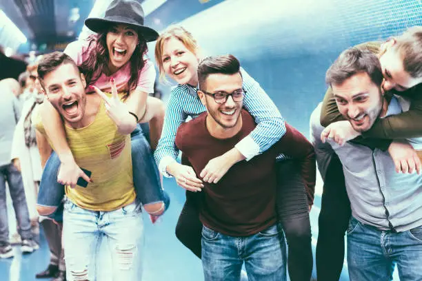 Group of friends having fun in underground metropolitan station - Young people hanging out ready for party night - Friendship and youth lifestyle concept - Focus on center girl face