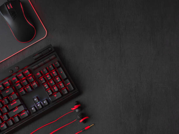 gamer workspace concept, top view a gaming gear, mouse, keyboard, joystick, headset, mobile joystick, in ear headphone and mouse pad on black table background.