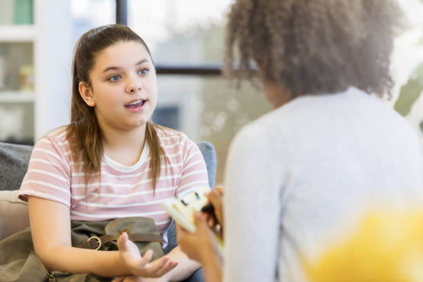 Teenage girl talks to school counselor A serious teenage girl gestures as she sits on a couch in her school counselor's office and talks to her unrecognizable counselor.  The counselor takes notes on a clipboard. mental health kids stock pictures, royalty-free photos & images