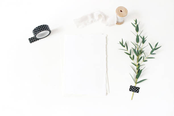 istock Feminine stationery, wedding desktop mock-up scene. Blank greeting card, envelope,black washi tape, silk ribbon and green Eucalyptus parvifolia branch.White table background. Flat lay, top view. 1051258764