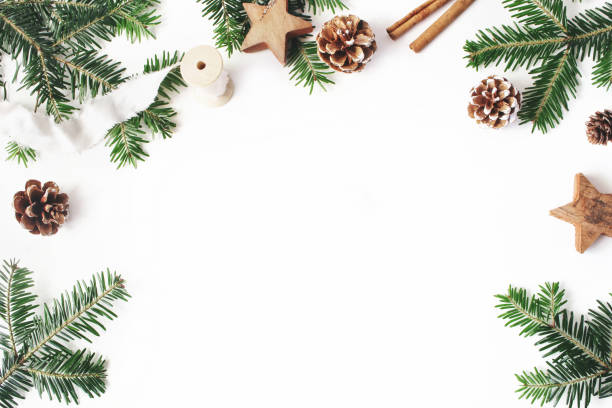 istock Christmas festive styled stock composition. Decorative floral frame. Fir tree branches border. Pine cones, wooden stars, cinnamon and ribbon on white wooden background. Flat lay, top view. Copy space. 1051258828