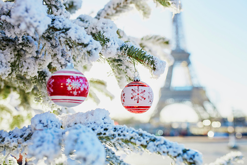 Christmas tree covered with snow and decorated with red toys near the Eiffel tower in Paris, France