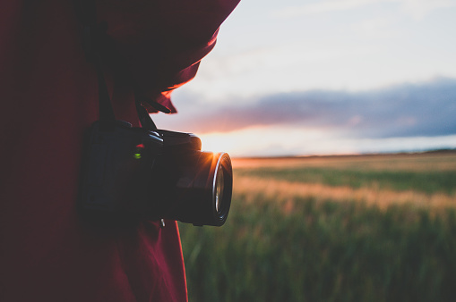 The woman with a retro camera against the background of a sunset in the wheat field