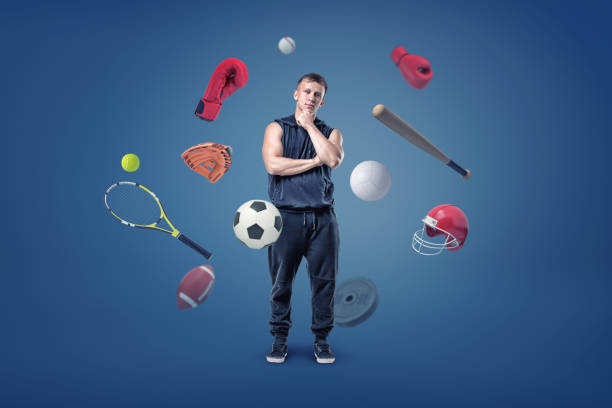 A thoughtful muscular man stands surrounded by different sport gear flying around him.