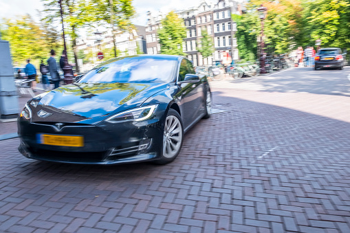 Tesla Model S full-sized electric five-door hatchback car driving along a canal in Amsterdam. Image with strong motion blur.